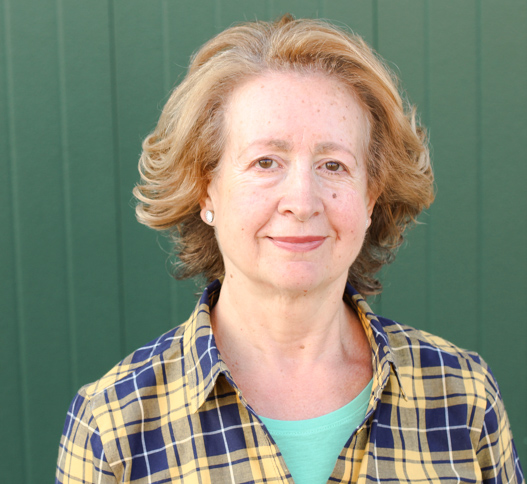 middle aged woman wearing a shirt standing in front of a green wall 